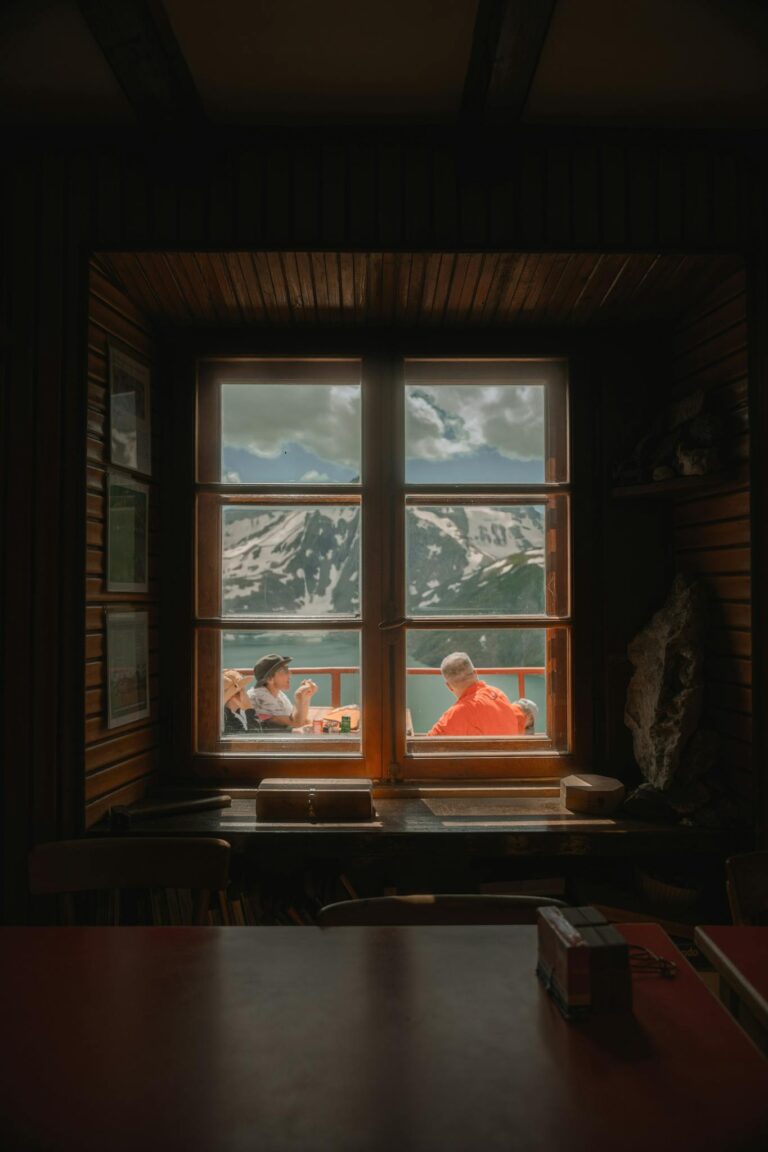 A serene view through a cabin window overlooking snowy peaks in Piemonte, Italy.
