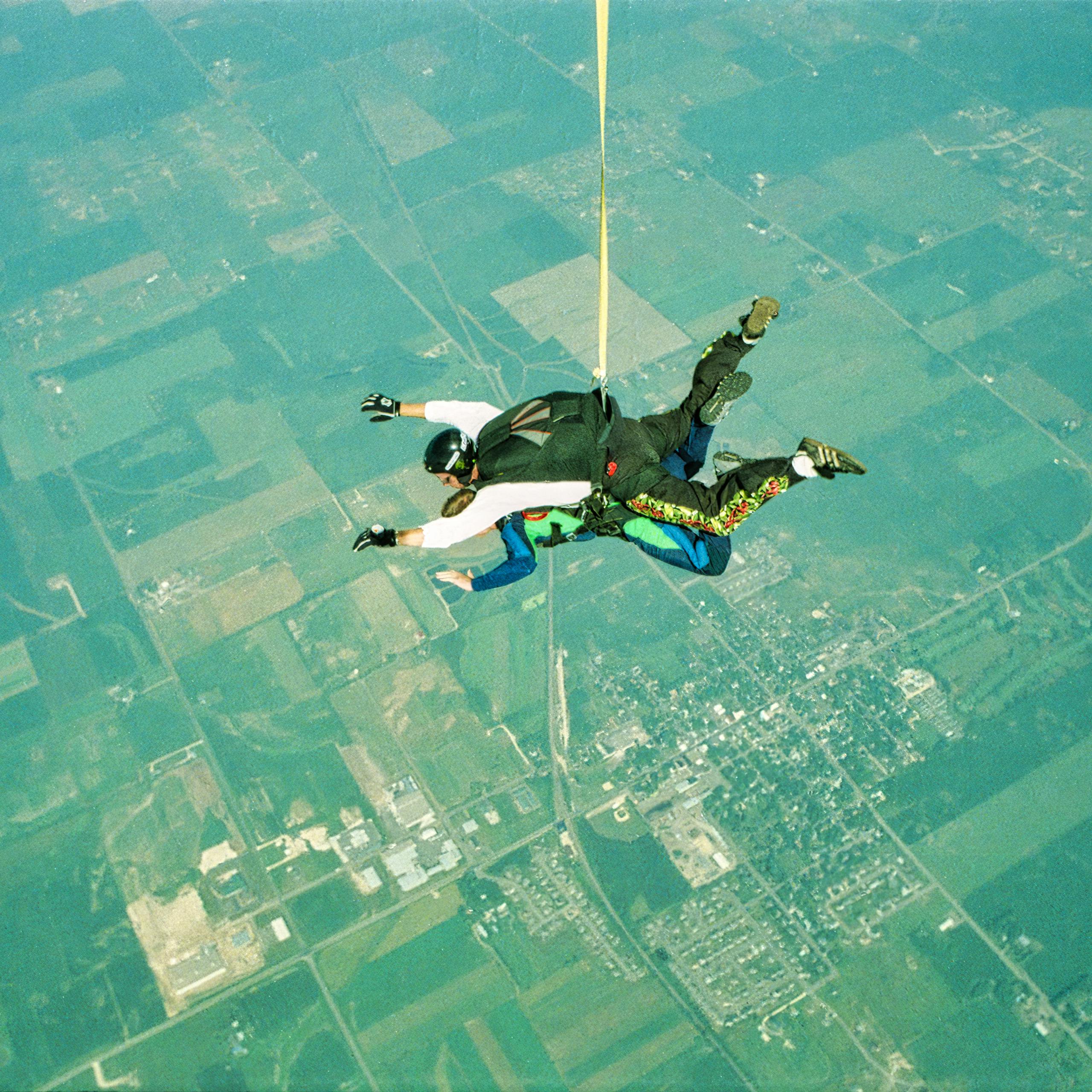 Two skydivers tandem over an urban landscape on a sunny day.